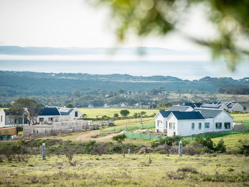 An elevated view of a residential development featuring modern homes with solar panels, set within a scenic landscape overlooking the distant coastline.