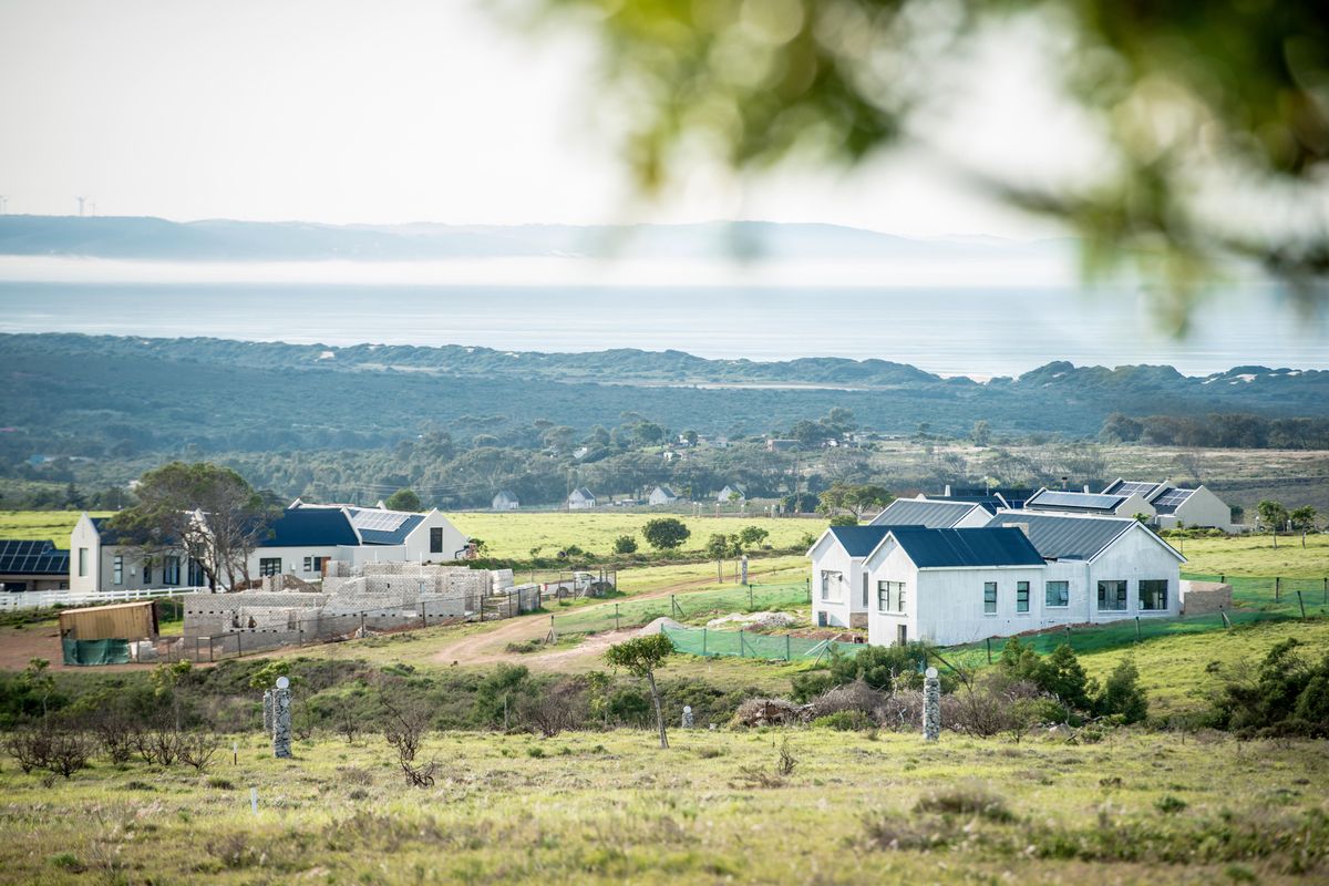 An elevated view of a residential development featuring modern homes with solar panels, set within a scenic landscape overlooking the distant coastline.