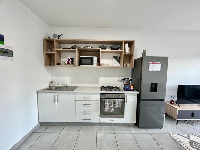 Compact kitchen featuring white cabinetry, open wooden shelving, a gas hob, built-in oven, and a stainless steel sink with tiled flooring.