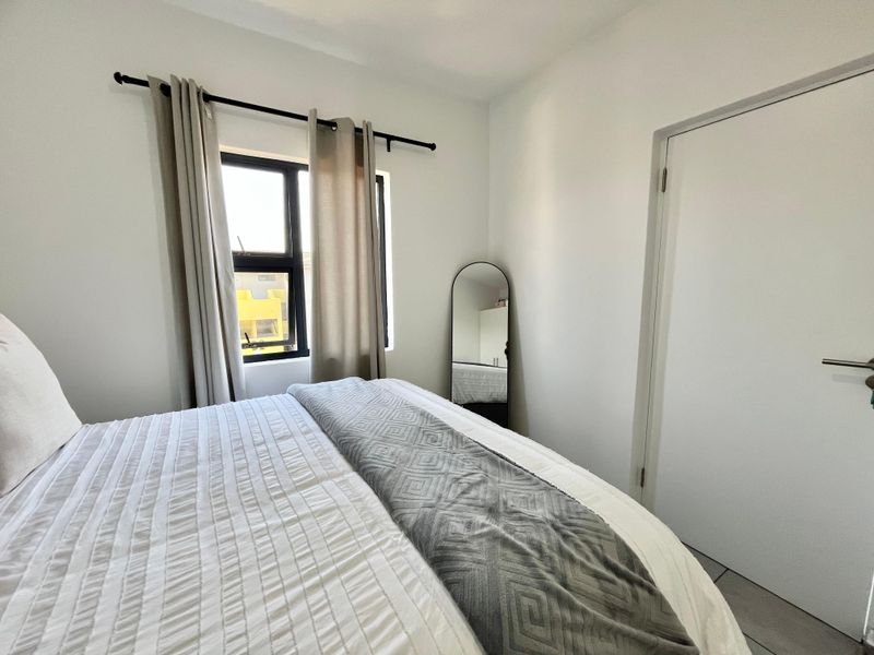 A clean and well-maintained bedroom featuring neutral walls, tiled flooring, and an aluminium-framed window with curtain rod.