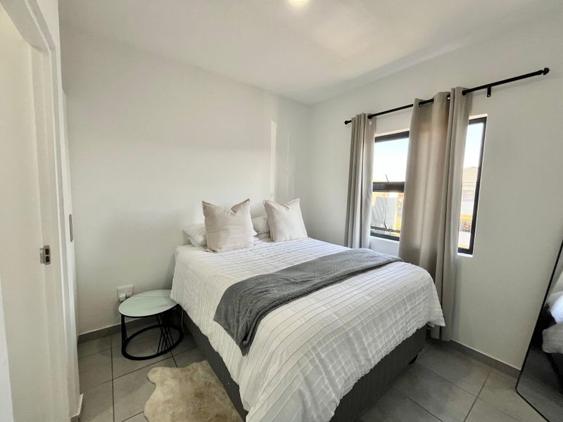 A clean and well-maintained bedroom featuring tiled flooring, a built-in cupboard, and a window with a curtain rod.