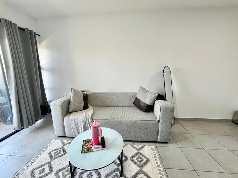 A bright living room featuring neutral tiled flooring and a large sliding glass door providing access to the outdoor area.