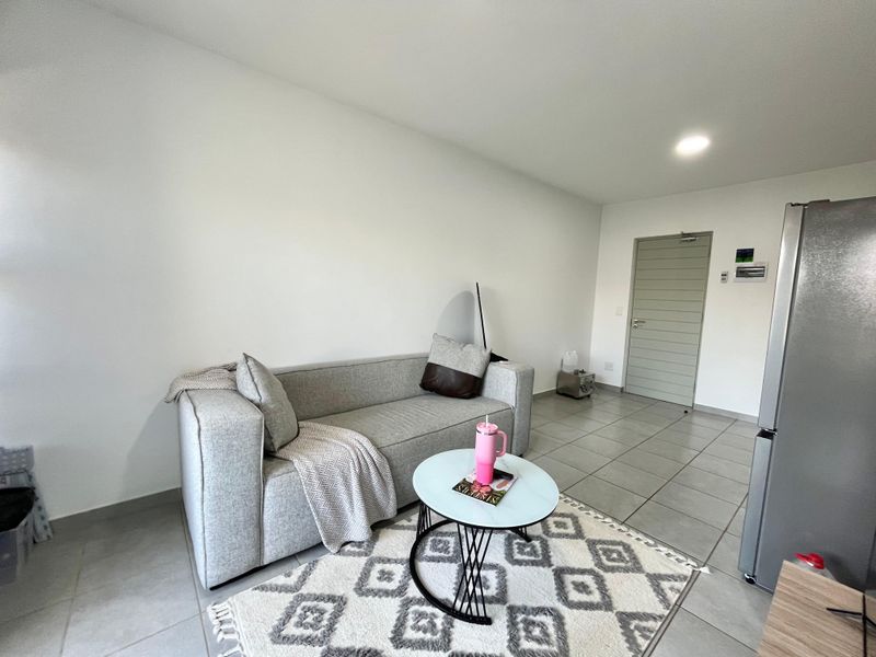 A bright, open-plan living area featuring neutral tiled flooring, recessed lighting, and a clean, modern aesthetic.