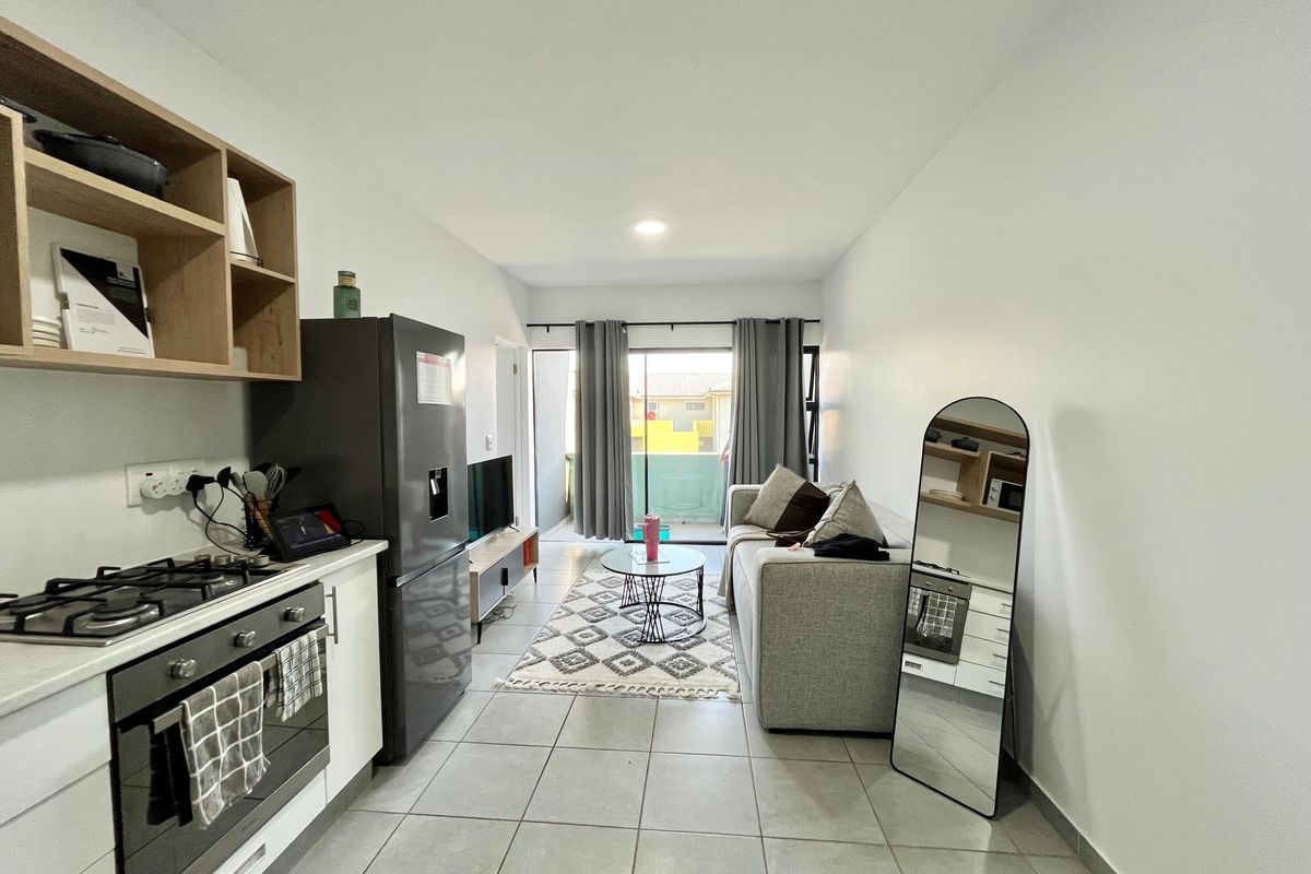Modern open-plan living area featuring a compact kitchen with built-in oven and gas hob, flowing into a lounge space with access to a balcony.