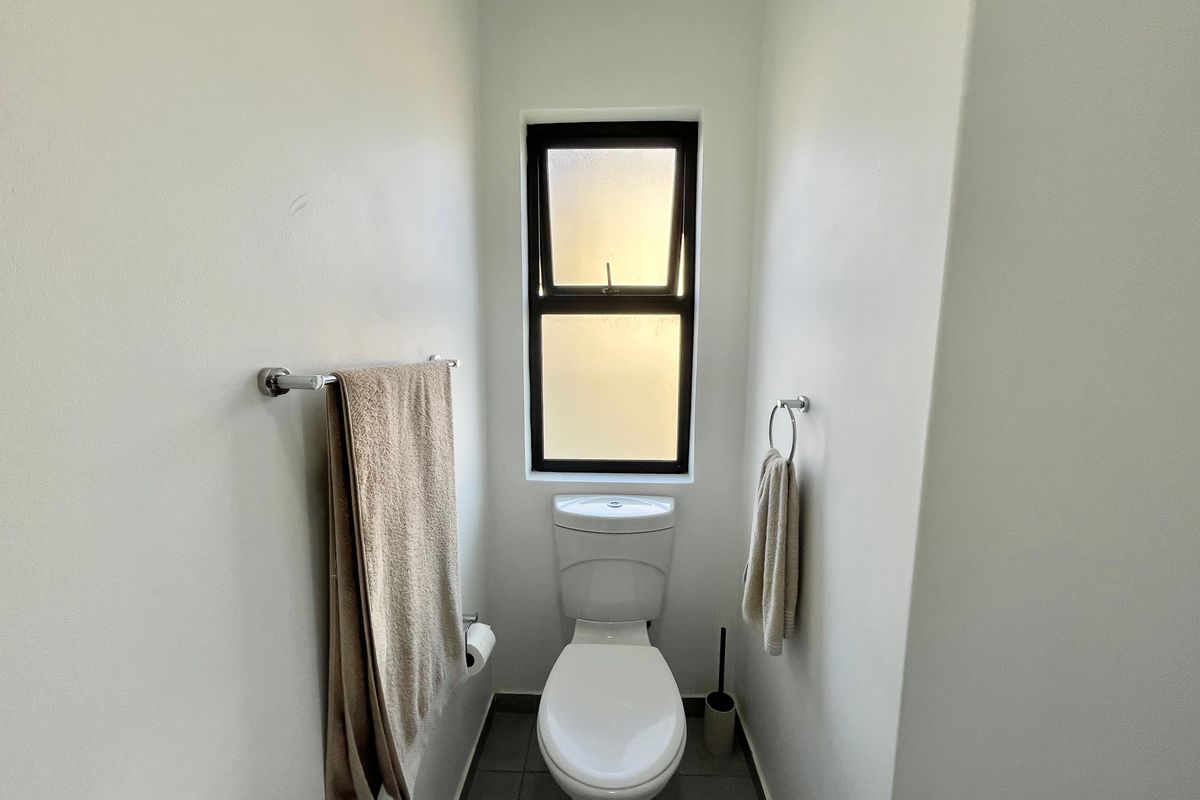 A clean and functional guest bathroom featuring a modern toilet, tiled flooring, and a frosted glass window for privacy.