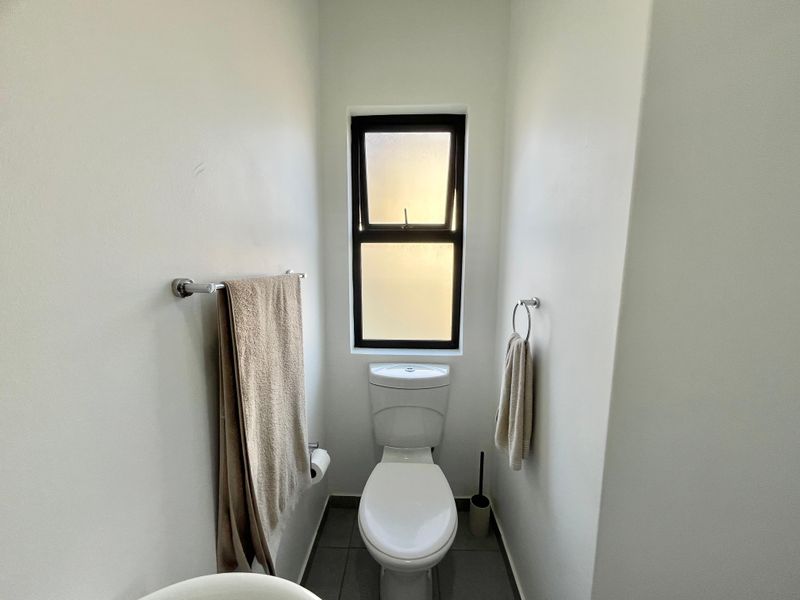 A clean and functional guest bathroom featuring a modern toilet, tiled flooring, and a frosted glass window for privacy.