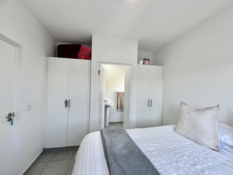 A clean bedroom featuring built-in cupboards and direct access to an en-suite bathroom with a pedestal basin.