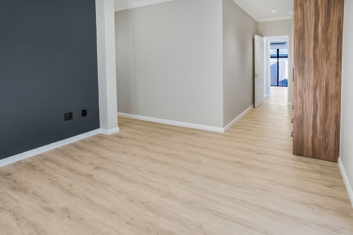 A bright, modern, and empty living area featuring light wood-look laminate flooring, a dark accent wall, and integrated cabinetry.