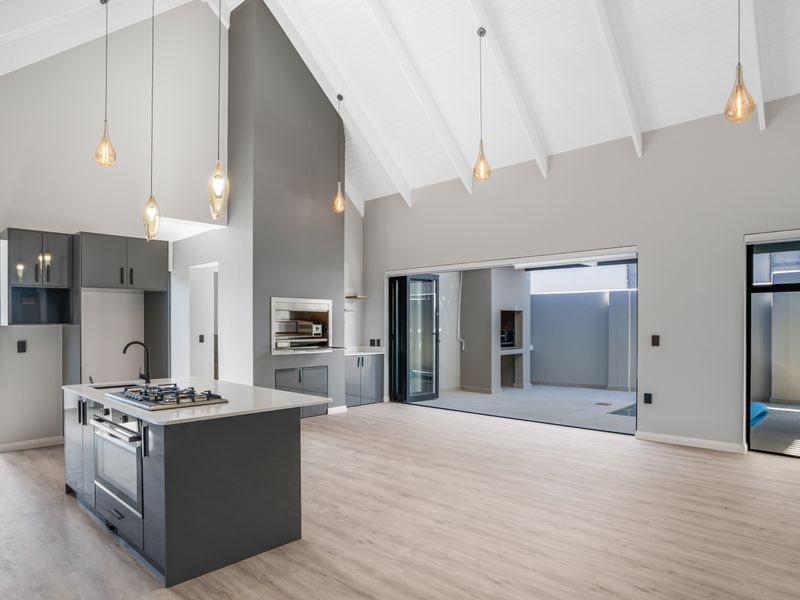 Spacious open-plan living area featuring a modern kitchen with island, vaulted ceilings, and seamless flow to the outdoor patio through large stacking doors.