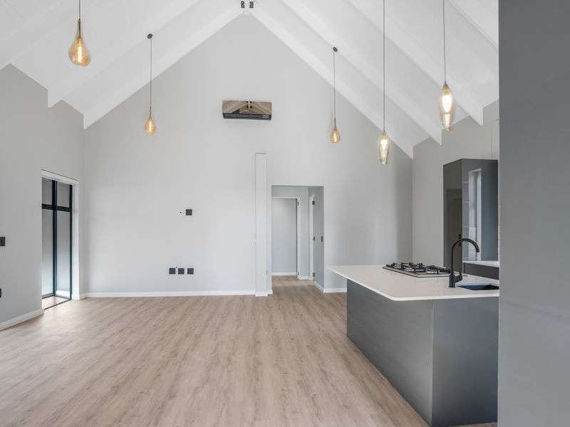 Spacious open-plan living area featuring a vaulted ceiling with exposed rafters, modern kitchen island with gas cooktop, and contemporary pendant lighting.