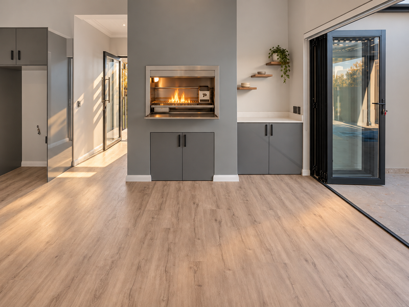 Modern indoor-outdoor entertainment area featuring a built-in braai, sleek grey cabinetry, and large stacking doors opening to the patio.