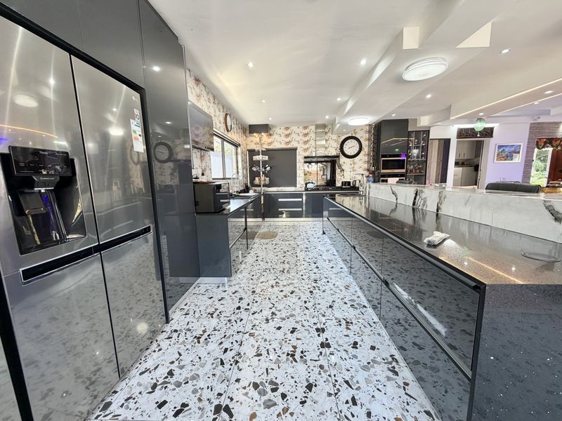 Modern kitchen featuring high-gloss cabinetry, stone countertops, a large central island, and distinctive terrazzo flooring with integrated lighting.