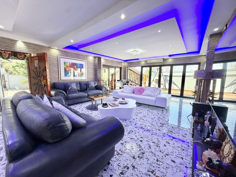 Spacious living room featuring a modern recessed ceiling with ambient LED lighting, stone-clad feature walls, polished terrazzo-style flooring, and large bi-fold doors leading outdoors.