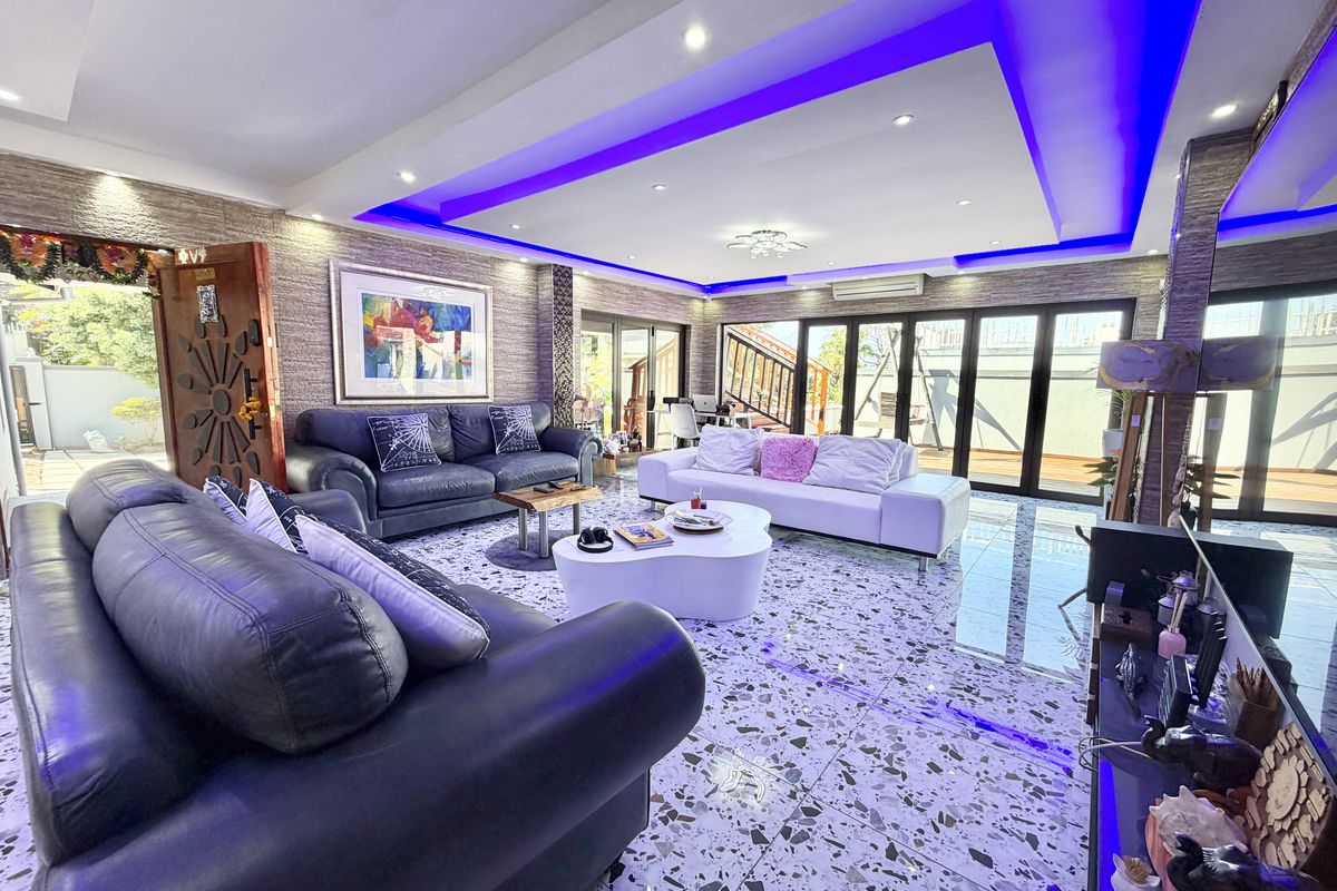 Spacious living room featuring a modern recessed ceiling with ambient LED lighting, stone-clad feature walls, polished terrazzo-style flooring, and large bi-fold doors leading outdoors.