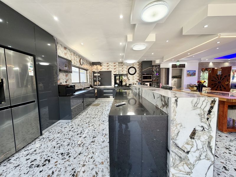 Modern kitchen featuring high-gloss cabinetry, a large stone-topped island, terrazzo flooring, and integrated appliances with recessed ceiling lighting.