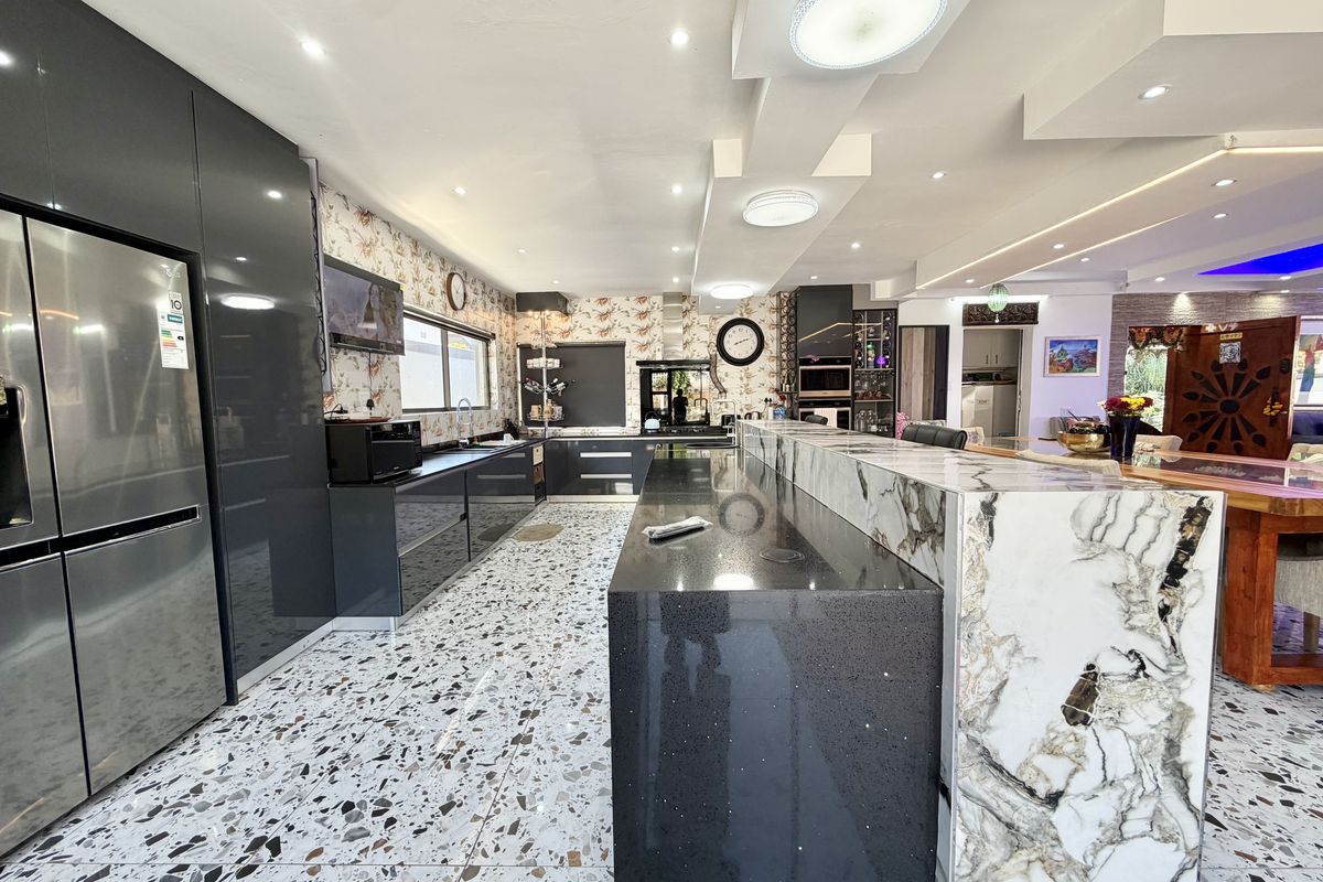 Modern kitchen featuring high-gloss cabinetry, a large stone-topped island, terrazzo flooring, and integrated appliances with recessed ceiling lighting.