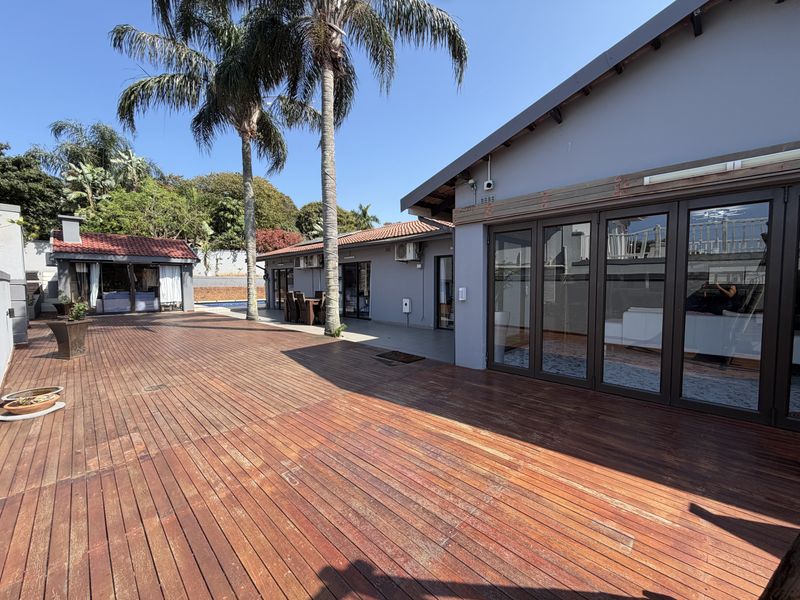Spacious outdoor timber deck featuring large stacking glass doors, providing seamless indoor-outdoor flow to the rear garden and pool area.