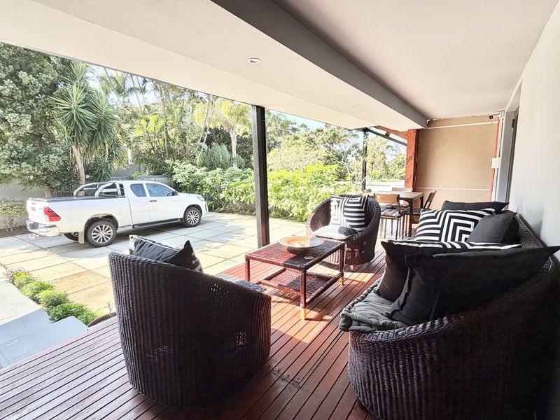 Covered outdoor patio featuring timber decking and recessed lighting, providing a functional space for relaxation overlooking the driveway and garden area.