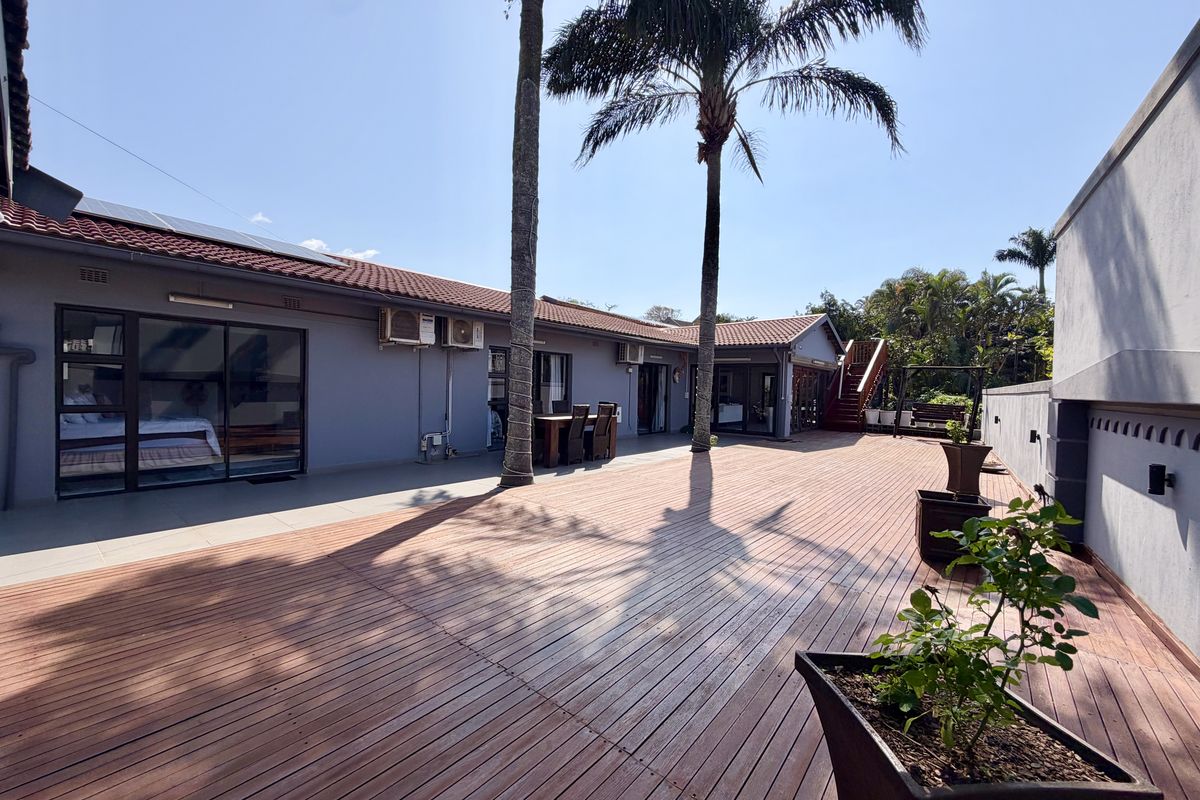 Spacious rear exterior featuring extensive timber decking, sliding glass doors providing indoor-outdoor flow, and a well-maintained tiled roof with solar panels.