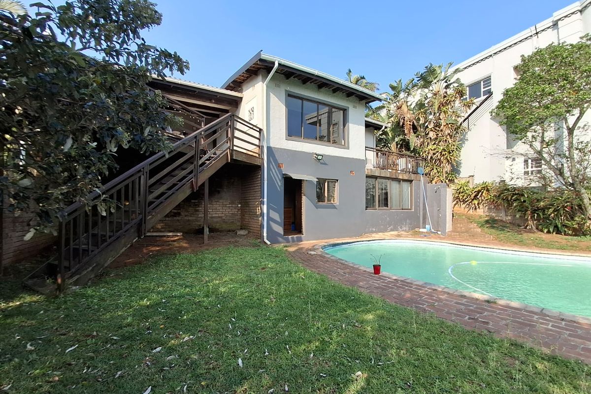 Rear exterior view of the house featuring a swimming pool, brick pool surround, and an elevated timber deck with an external staircase.