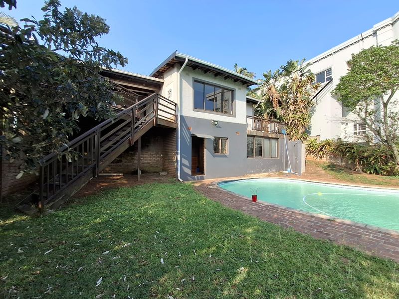 Rear exterior view of the house featuring a swimming pool, brick pool surround, and an elevated timber deck with an external staircase.