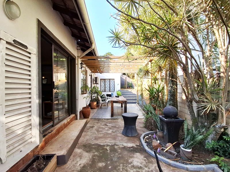 A covered patio area featuring a wooden pergola, tiled flooring, and sliding glass door access to the interior, set within a landscaped garden space.