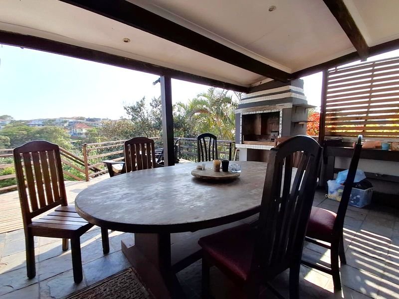 Covered outdoor patio featuring a built-in braai, timber decking, and elevated views, providing a functional space for outdoor dining and entertainment.