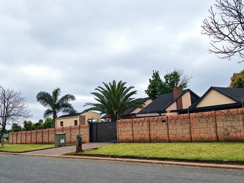 Front view of the property featuring a secure perimeter wall, metal gate, tiled roof, and established garden landscaping.