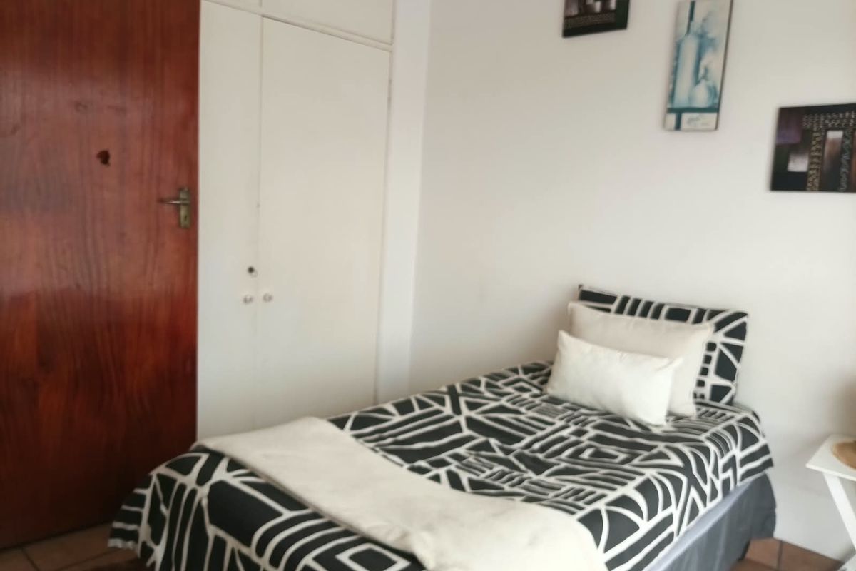 A bedroom featuring built-in cupboards, tiled flooring, and a solid wood door, offering a functional space with potential for cosmetic updates.
