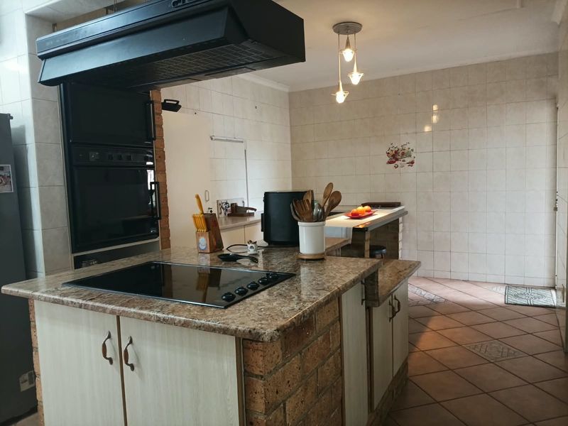 A functional kitchen featuring a brick-based island with a granite countertop, built-in oven, extractor fan, and tiled finishes throughout.