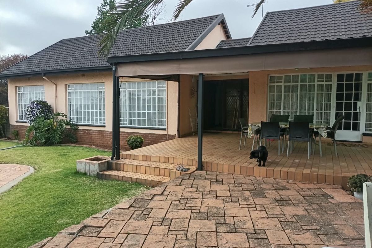 Rear view of the house featuring a covered tiled patio, brick paved area, and a well-maintained lawn with grid-pattern windows.