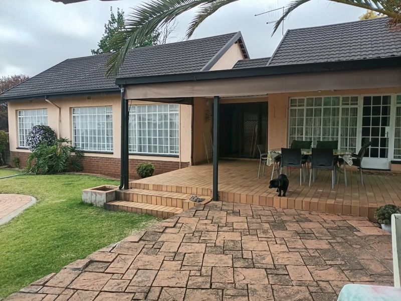 Rear view of the house featuring a covered tiled patio, brick paved area, and a well-maintained lawn with grid-pattern windows.
