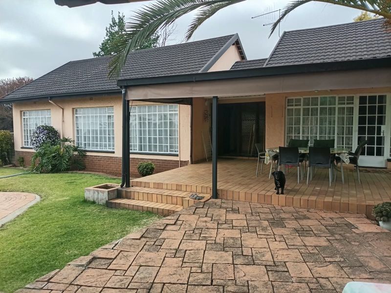 Rear view of the house featuring a covered tiled patio, paved courtyard area, and established garden space with security-barred windows.