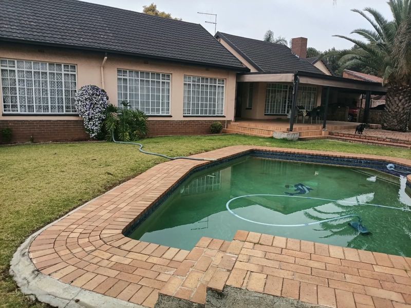 Rear view of the house featuring a swimming pool, brick paved surround, covered patio area, and established garden.