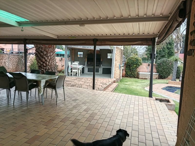 Spacious covered patio featuring a built-in braai area, overlooking a private garden and swimming pool, ideal for outdoor entertaining.