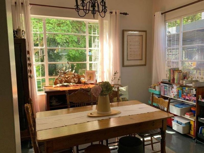A bright dining room featuring large steel-framed windows that provide ample natural light and views of the garden.