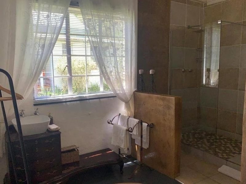 Bathroom featuring a walk-in shower with glass screen, pebble tile flooring, and a basin area with natural light from the window.