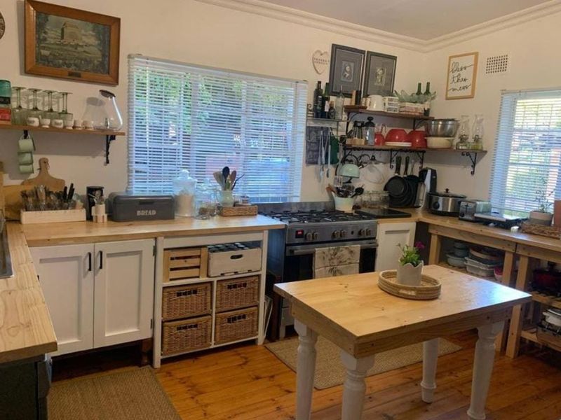 A rustic-style kitchen featuring timber countertops, gas stove, wooden flooring, and ample built-in cabinetry with a central island workspace.