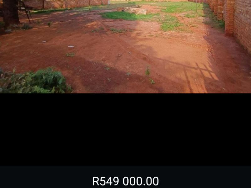 A vacant residential plot featuring a brick perimeter wall and open ground, offering a blank canvas for future development.