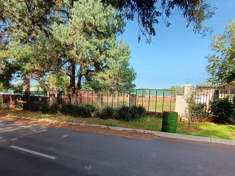Street view of the residential property showing the perimeter fencing, mature trees, and road frontage.