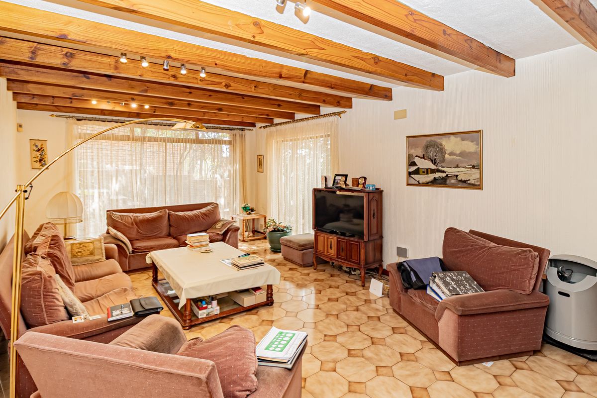 Spacious living room featuring exposed timber ceiling beams, ceramic tile flooring, and large sliding glass doors providing ample natural light.