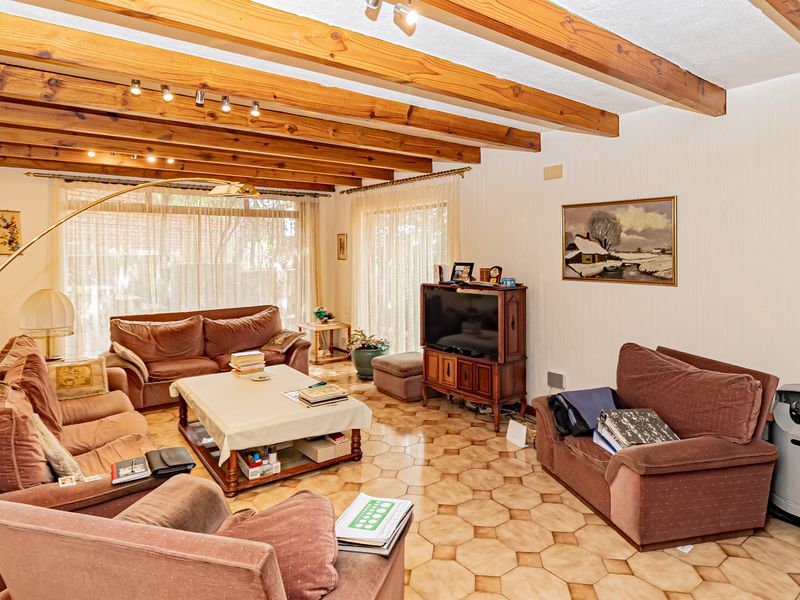 Spacious living room featuring exposed timber ceiling beams, ceramic tile flooring, and large sliding glass doors providing ample natural light.