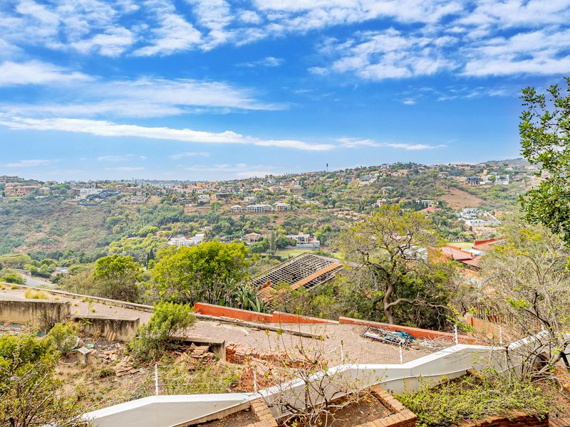 Elevated panoramic view overlooking the surrounding hillside and residential neighborhood, featuring tiered retaining walls and paved outdoor areas.