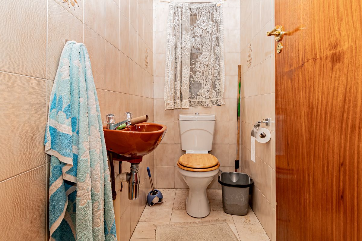 A compact guest bathroom featuring tiled walls and floors, a wall-mounted basin, and a standard toilet.