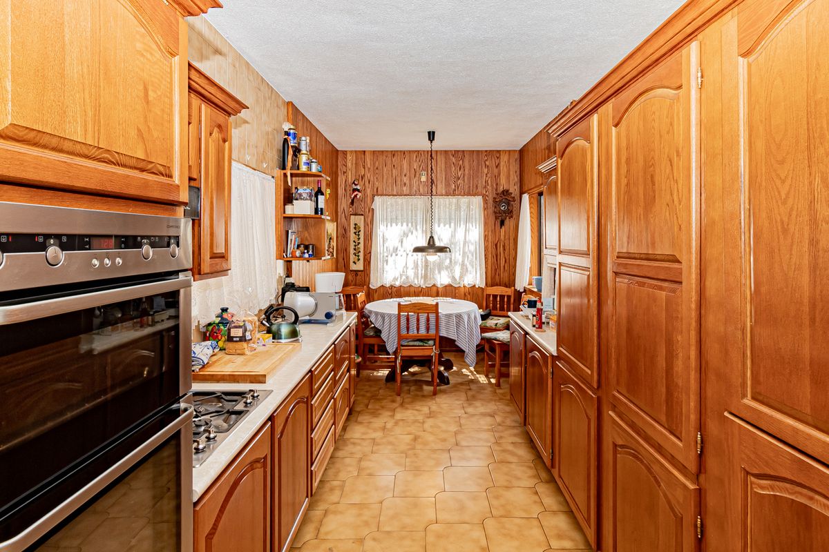 A traditional kitchen featuring extensive wooden cabinetry, built-in oven, gas hob, and tiled flooring, with an integrated dining area at the rear.