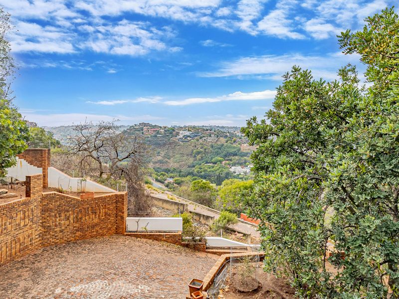 An elevated outdoor view featuring brick retaining walls, a cobblestone driveway, and expansive hillside landscape vistas.
