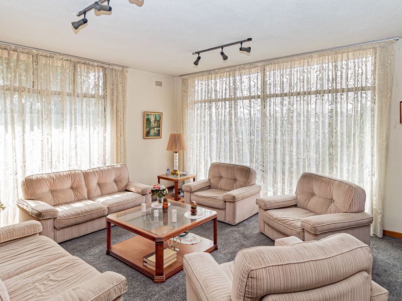 A spacious living room featuring large floor-to-ceiling windows that provide ample natural light, complemented by track lighting and carpeted flooring.