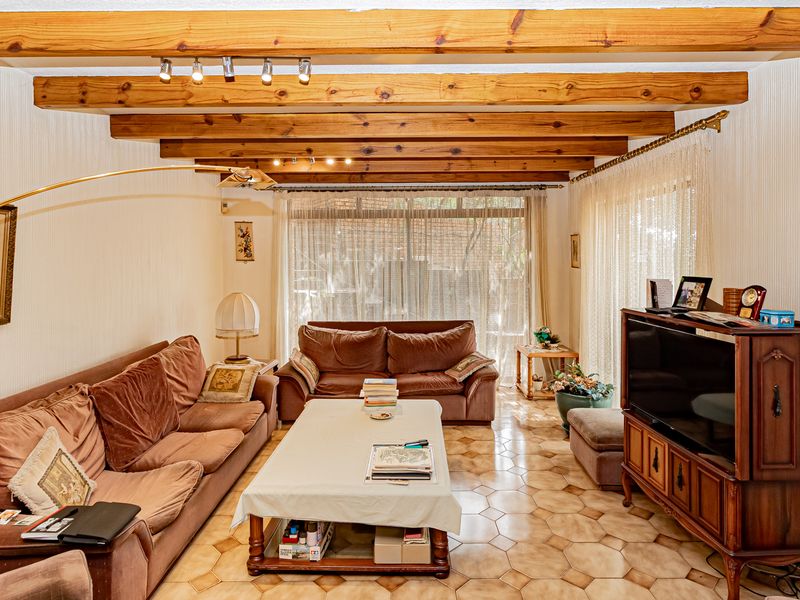 A cozy living room featuring exposed timber ceiling beams, tiled flooring, and large sliding glass doors that provide ample natural light.