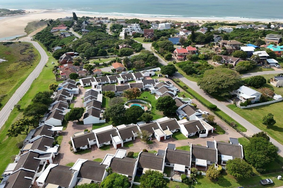 Aerial view of a coastal townhouse complex featuring uniform residential units, communal pool, and landscaped grounds, situated near the beach.