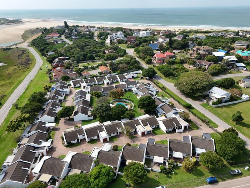 Aerial view of a coastal townhouse complex featuring uniform residential units, communal pool, and landscaped grounds, situated near the beach.